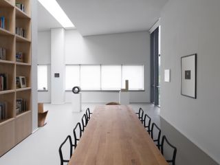 Long wooden table, black framed chairs and wooden shelving unit against wall