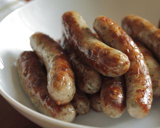 A white bowl containing a number of cooked sausage links