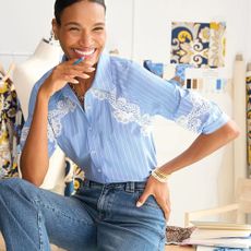 A woman sitting on a desk wearing a white and blue pinstriped shirt with lace detailing and high-waisted denim jeans from Talbots