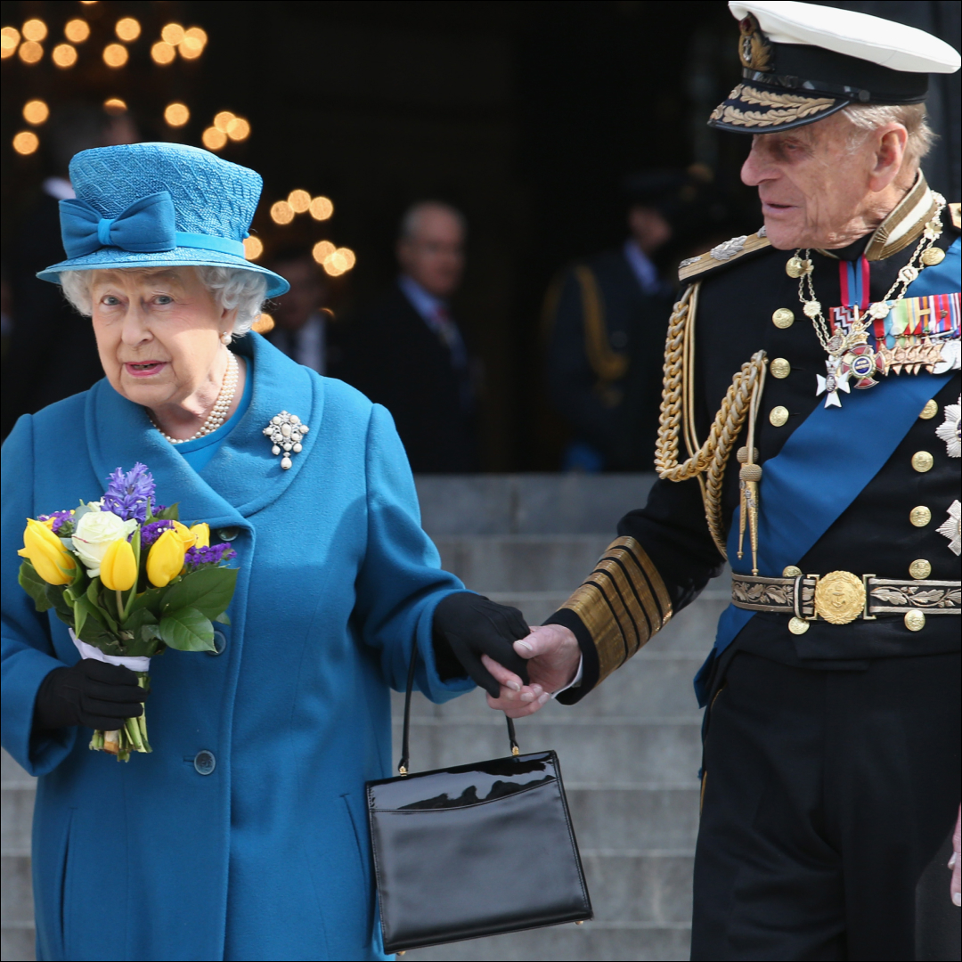 Queen Elizabeth wears a blue coat and matching hat and carries a bunch of tulips while her husband Prince Philip holds her hand