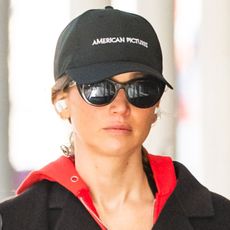Jennifer Lawrence wears a baseball cap, red sweatshirt, and sunglasses.
