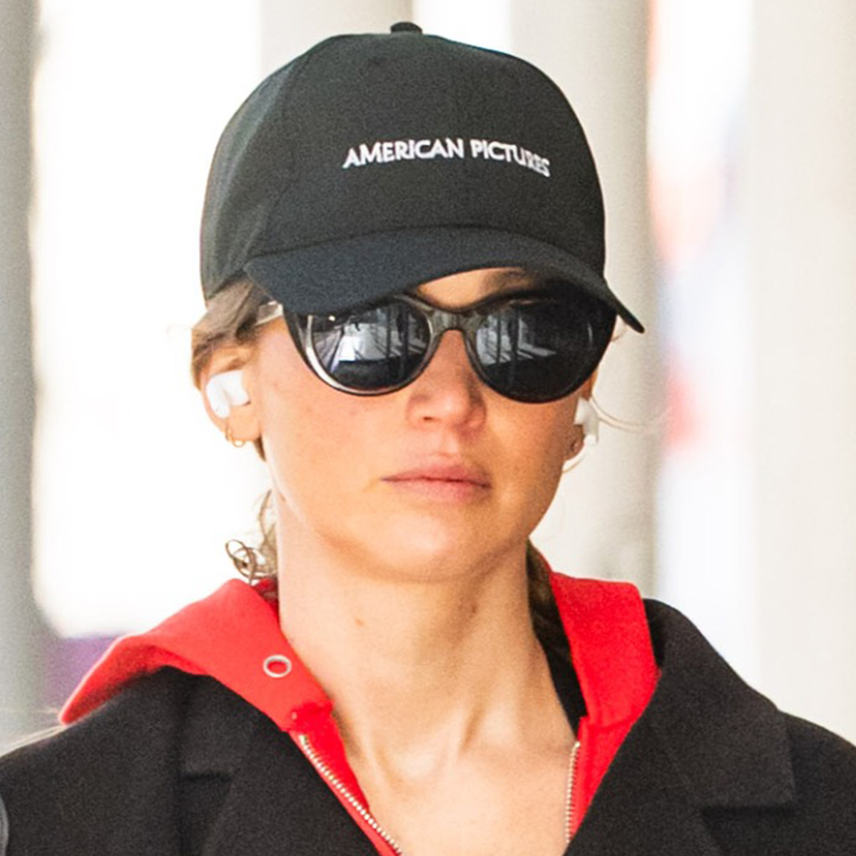 Jennifer Lawrence wears a baseball cap, red sweatshirt, and sunglasses.