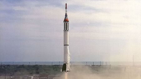 a white rocket with black stripes carrying a small back capsule launches.