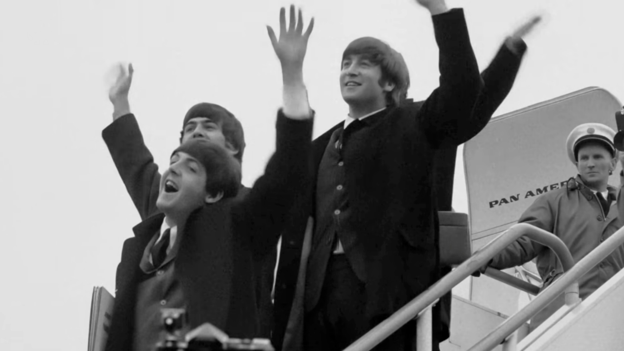 The Beatles waving on the stairs to an airplay in black and white.