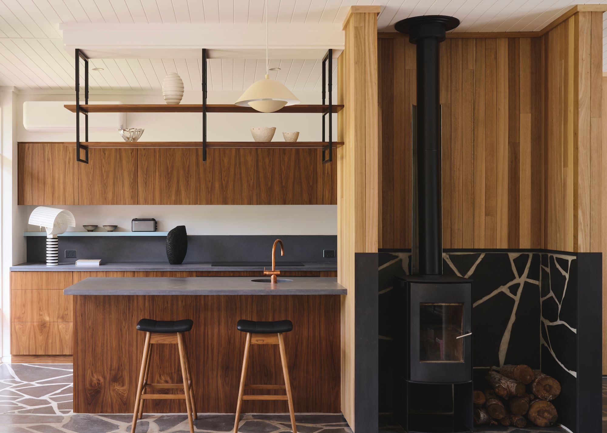 A kitchen with concrete flooring, stone counters, and wooden cabinets and island