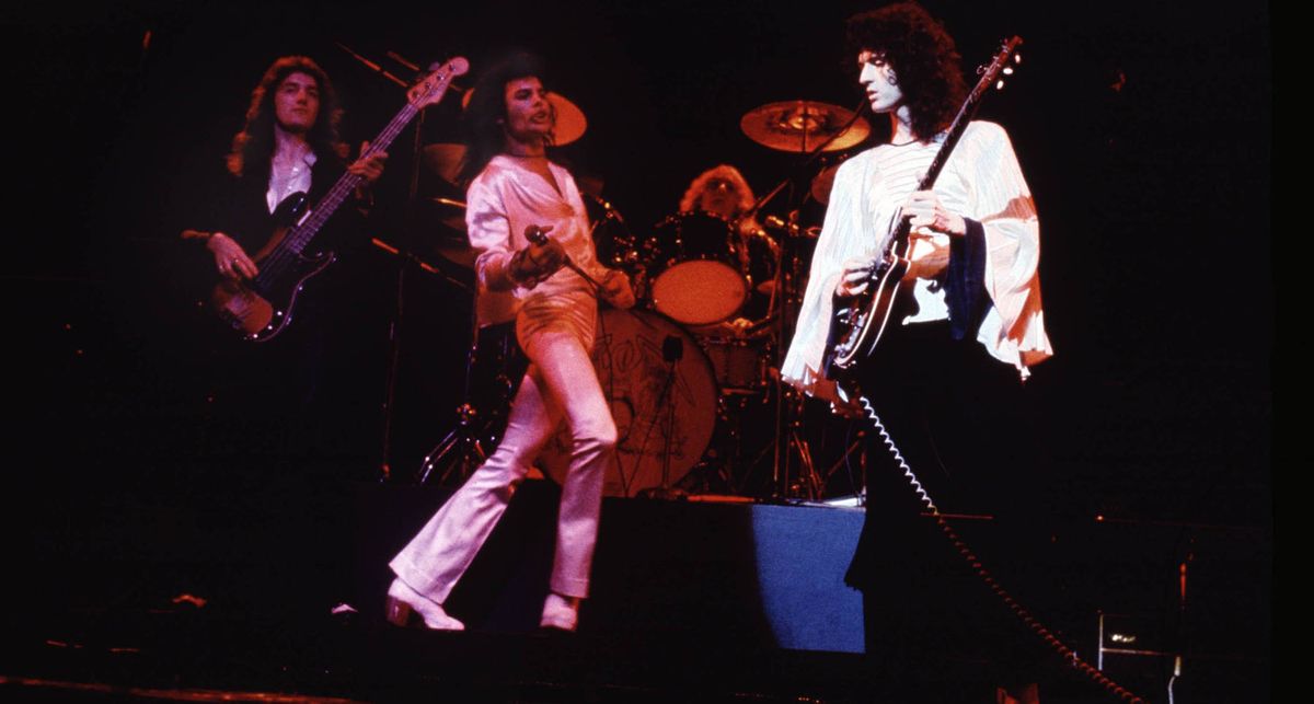 Queen live onstage in 1974, just after the release of their debut album. Brian May wears a white shirt and takes a solo on his Red Special electric guitar, John Deacon is holding it down on the P-Bass, while Freddie Mercury wears an all-white suit and waits to come in on vocals again.