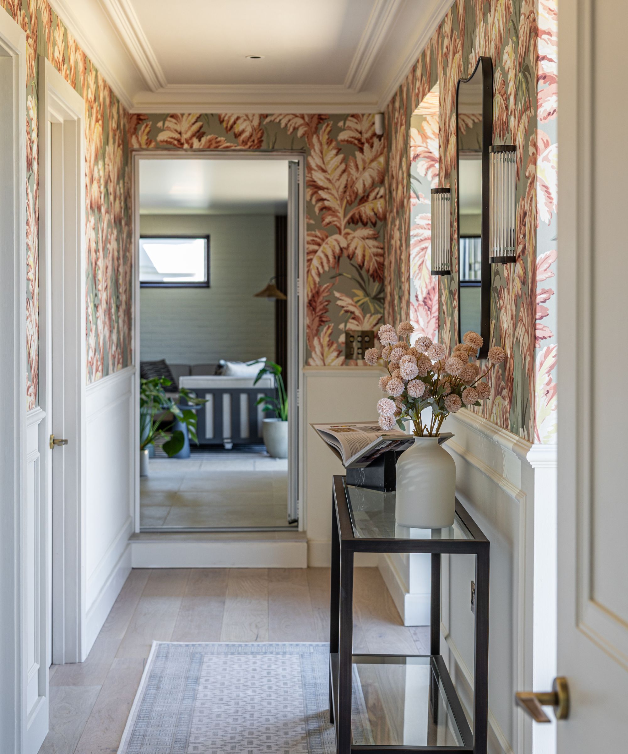 Elegant hallway with botanical wallpaper and classic panelling, styled with a glass console table, mirror and soft pastel tones throughout.