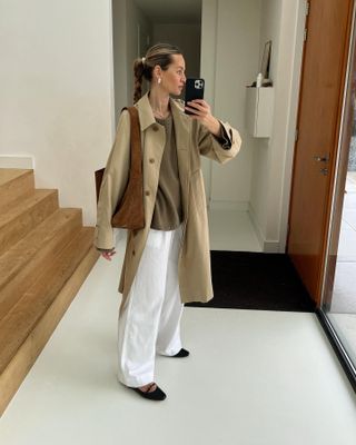 Anouk wears a trench coat, jumper, white linen trousers and flats