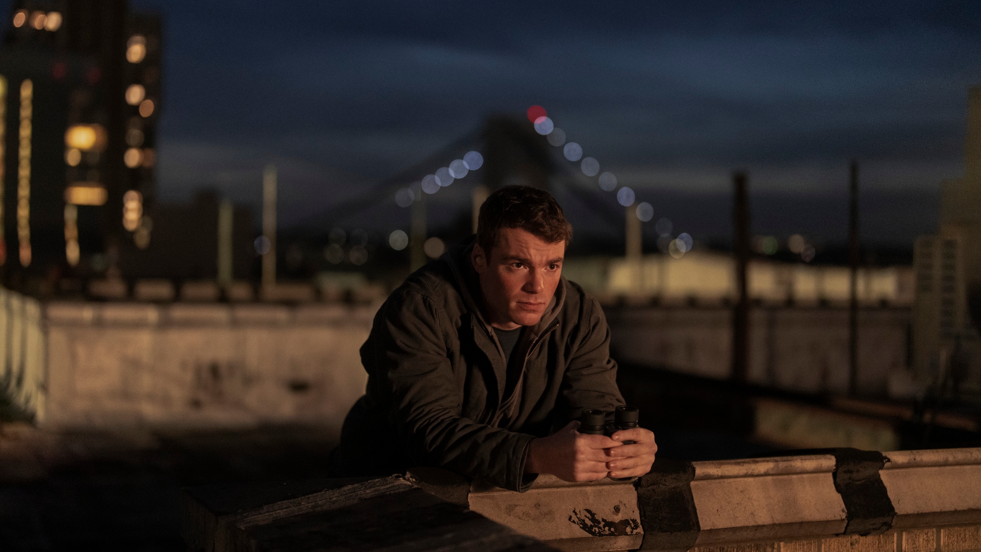 Peter leans over a bridge at night in The Night Agent