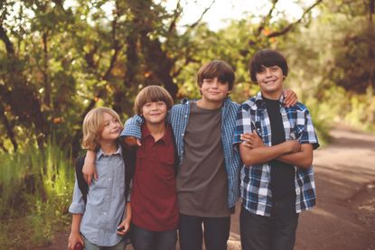 Four young brothers on the way to school. Looking into camera, smiling, happy, wearing back packs.