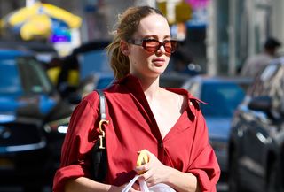 Jennifer Lawrence in NYC wearing a red oversize collared shirt with red pants, a black Dior Saddle bag, and orange slippers.