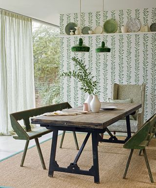 Dining room inspired by nature, with leaf pattern wallpaper, rustic upcycled dining table, bench seats and chair on hessian rug and green ceiling lights