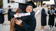 Two female students in graduation gowns embracing each other on the university campus