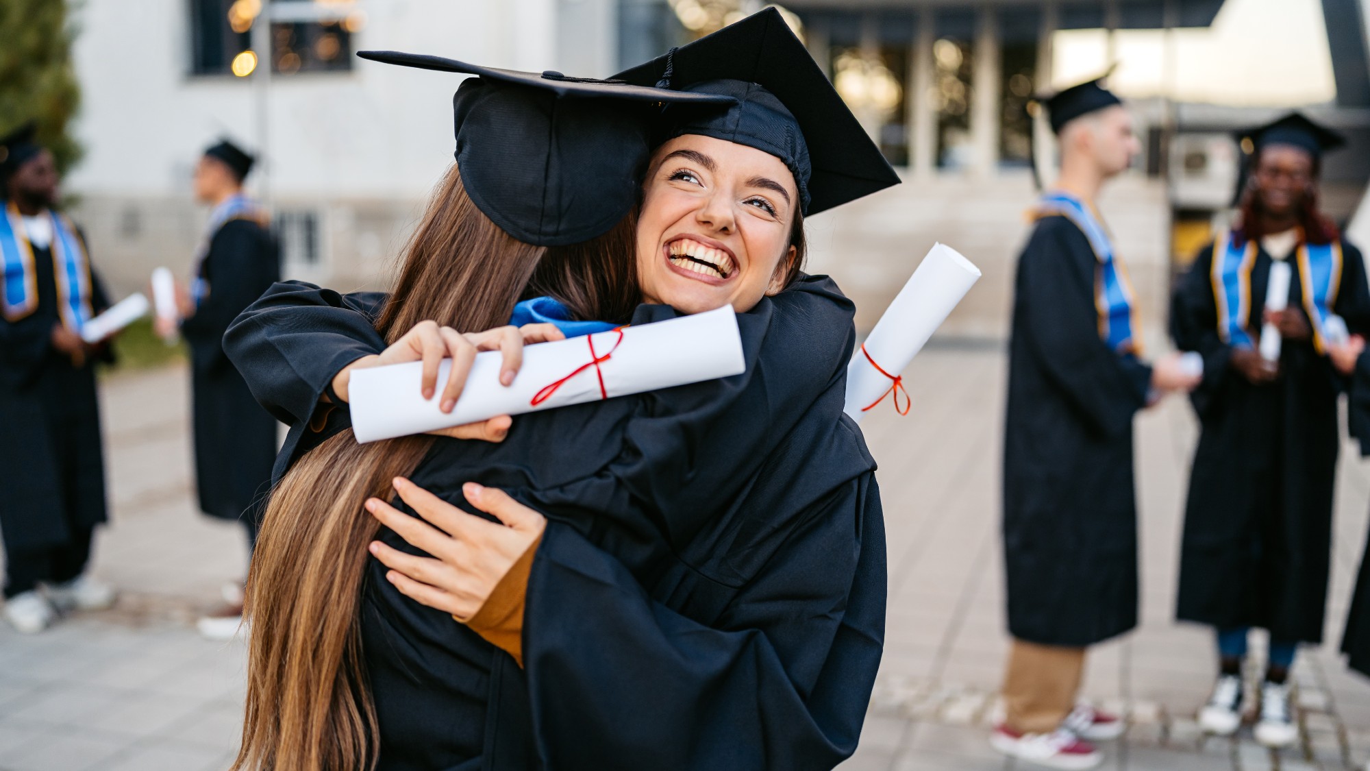 Two female students in graduation gowns embracing each other on the university campus