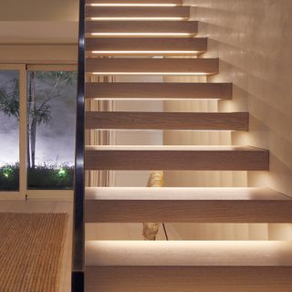 A modern wooden staircase with underlights in hallway with brown rug and sliding doors