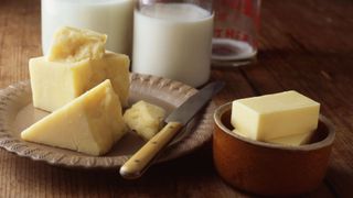 A selection of calcium-rich cheeses, including cheddar and parmesan, sitting on metal plate on wooden table next to beakers of milk