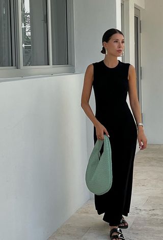 a woman's outfit showing what to wear in 80-degree weather with a black maxi dress styled with flat sandals and a woven leather shoulder bag