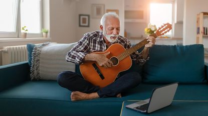 A man sits on his couch and plays the guitar.