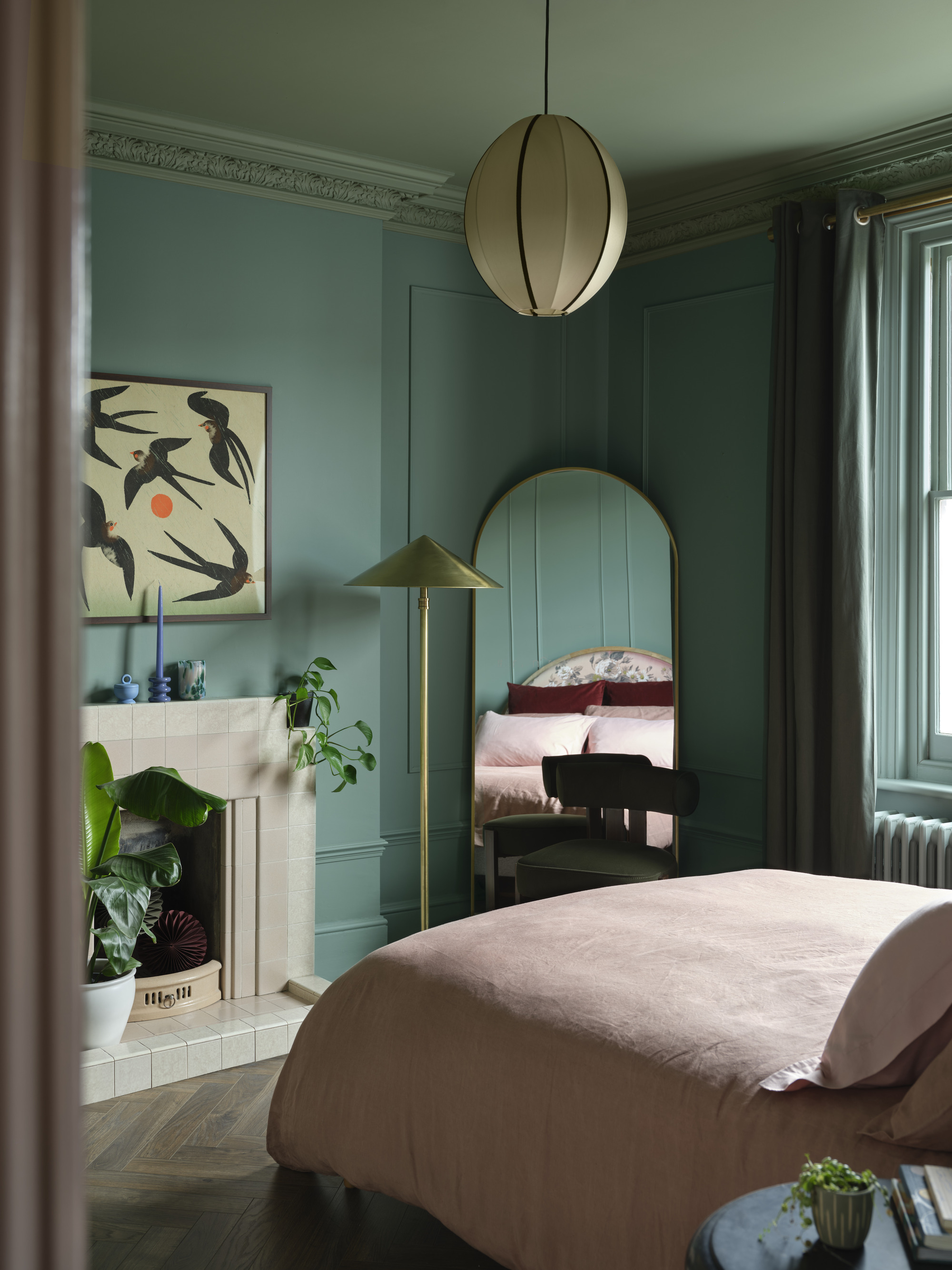 Image of a bedroom where the walls are painted in a color-capping technique using varying shades of dark teal paint. There is a bed with dusty pink bedding and a dull length mirror in the corner.