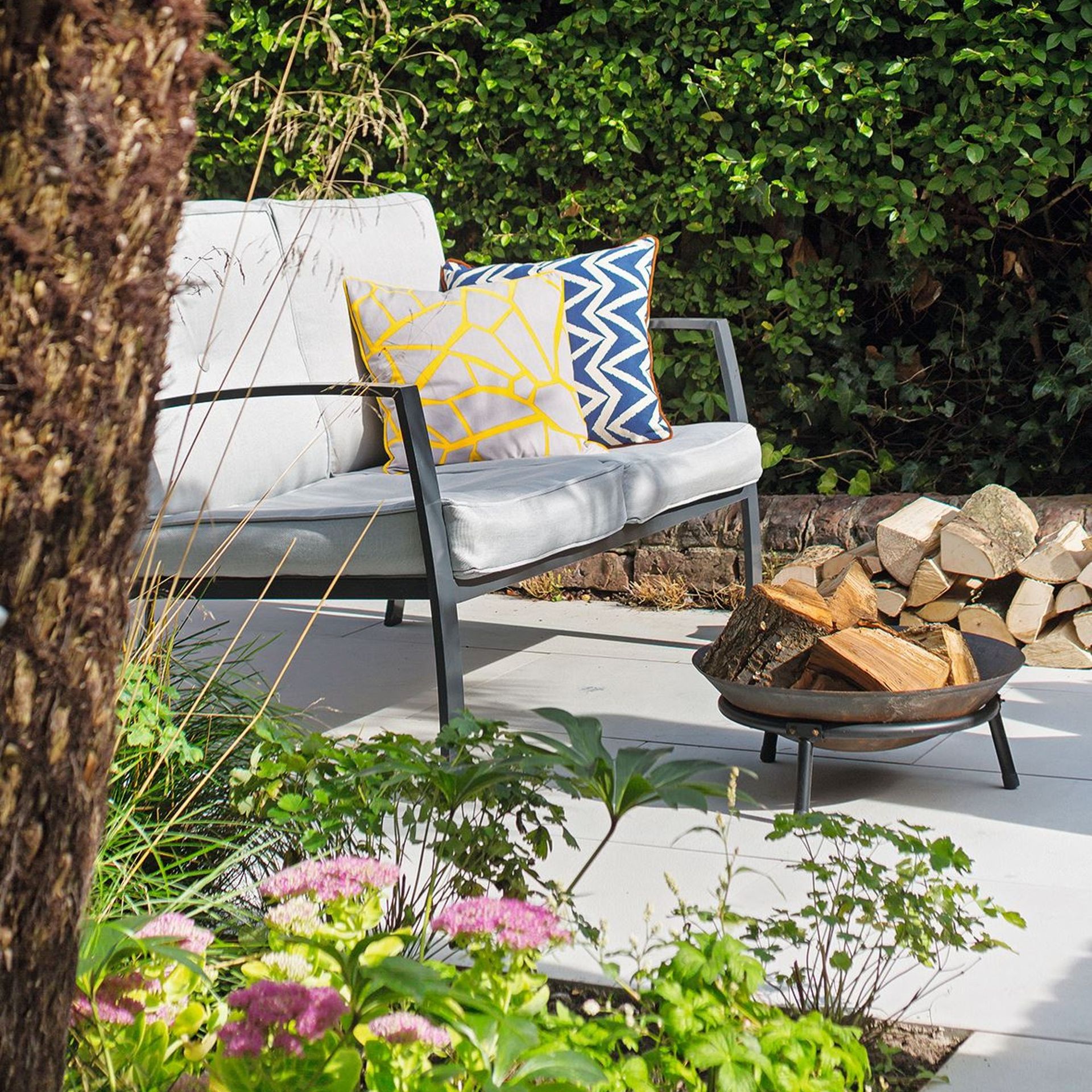 Outdoor sofa with colourful cushions on a stone path with a firepit