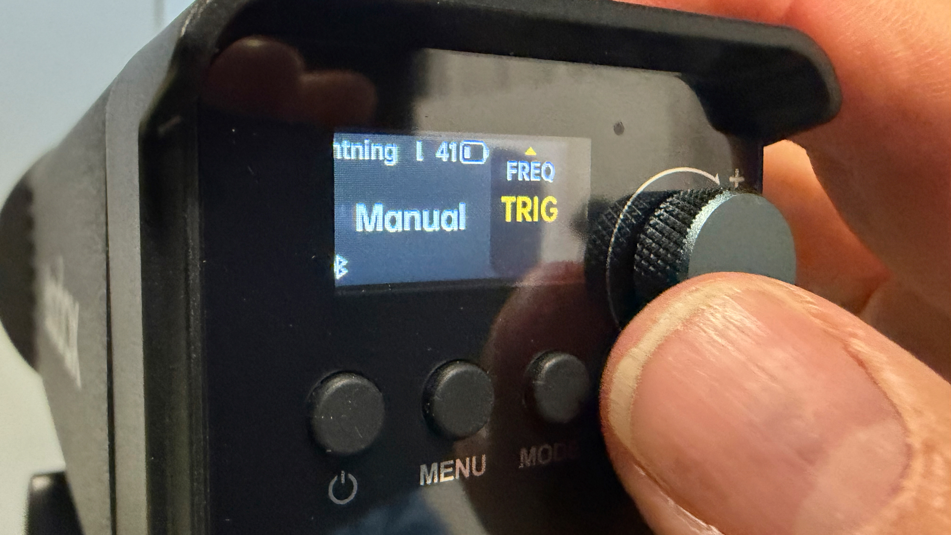 Shot of the rear of the RS100Bi showing a hand using the knob to adjust the properties of the Lightning animated effect. The various editable properties are displayed on a small OLED screen.