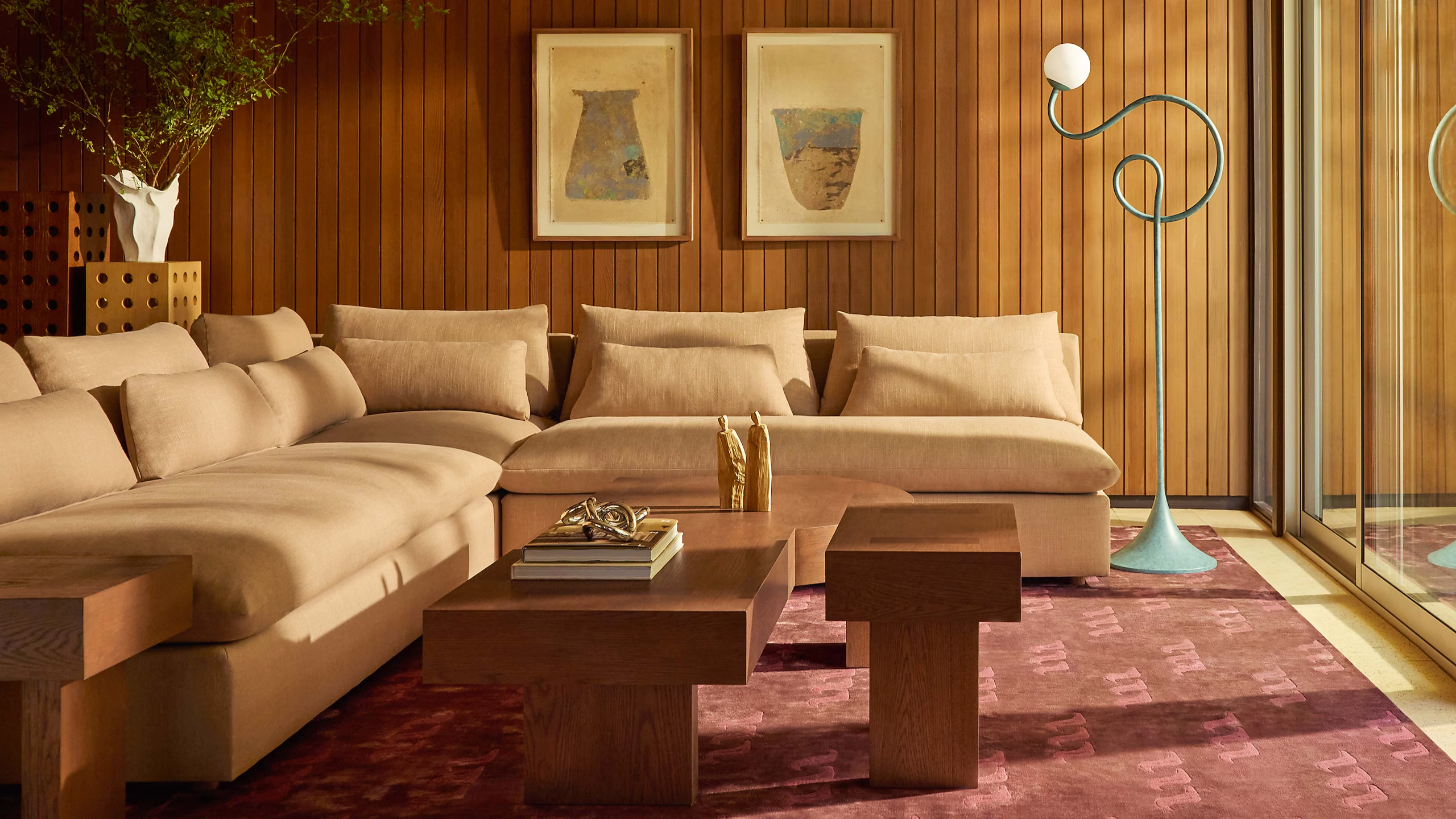 a sophisticated yet whimsical living room with a large tan sectional, wood paneled walls, a red rug, and a squiggle-inspired floor lamp