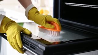 Person scrubbing the inside of an oven with a scourer brush and rubber gloves.