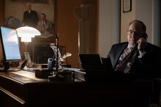 bill camp sits at a desk on the phone in a still from zero day