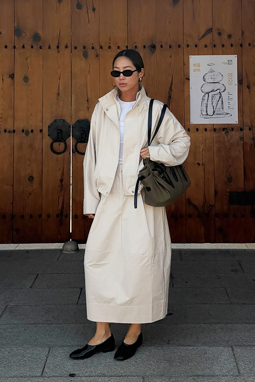 a woman wearing a tan jacket, tan skirt, and black flats