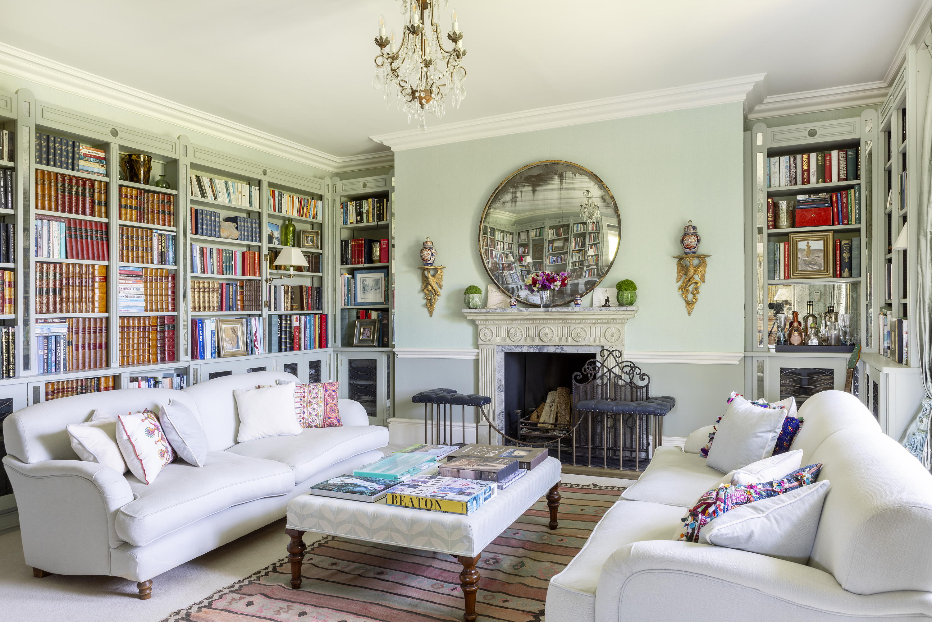 Mount Farm's living room with colourful bookshelves and a large circular mirror above an ornate fireplace 
