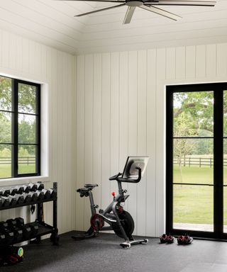 Home gym with white wooden panelling, weights and exercise bike