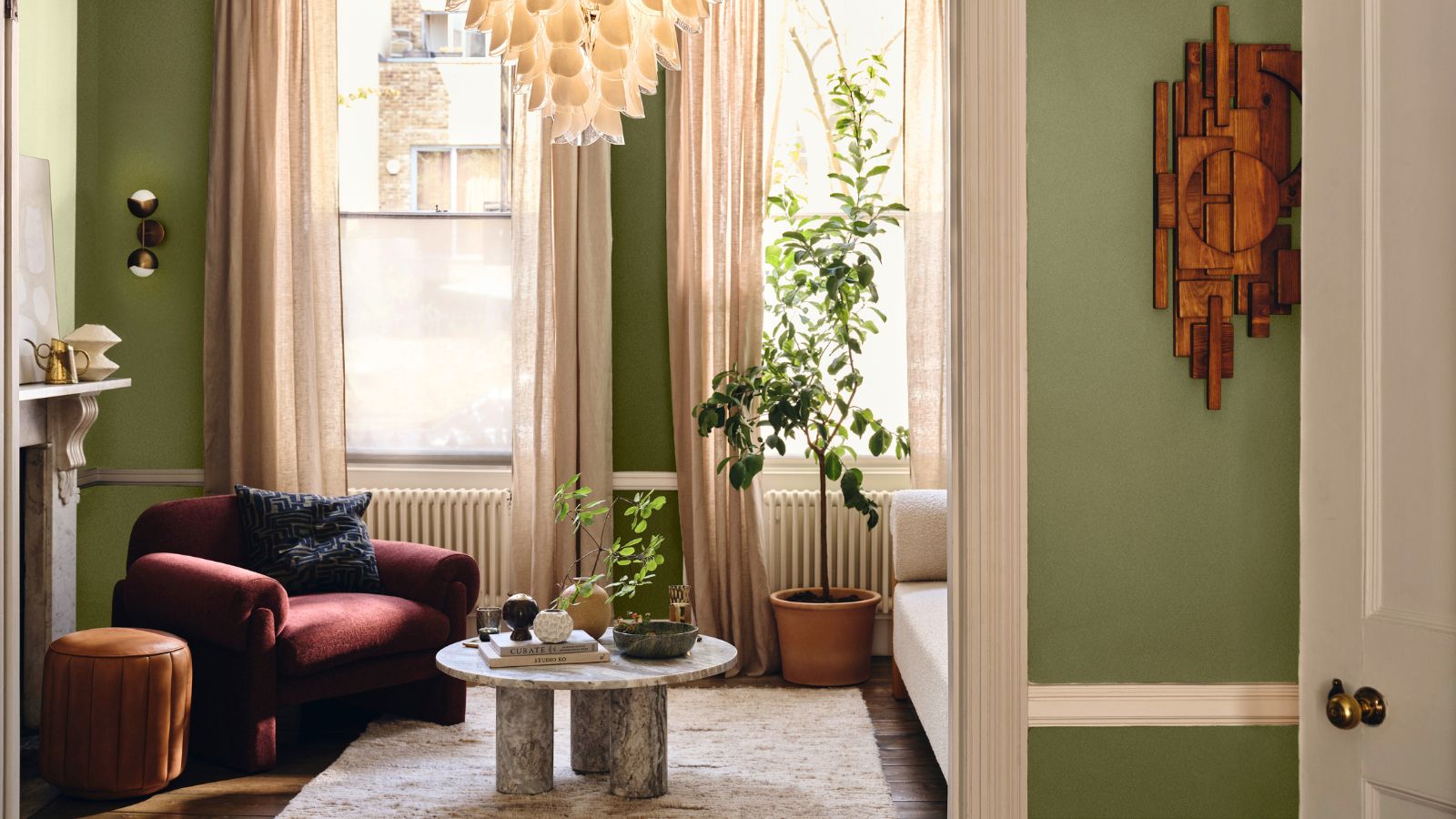 A cozy apartment living room with green painted walls. A red armchair in the far corner, a small round marble coffee table in front of it, and a cream rug. 