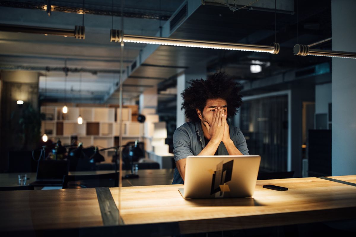 Office worker holding hands to face in frustration over workplace technology failure.