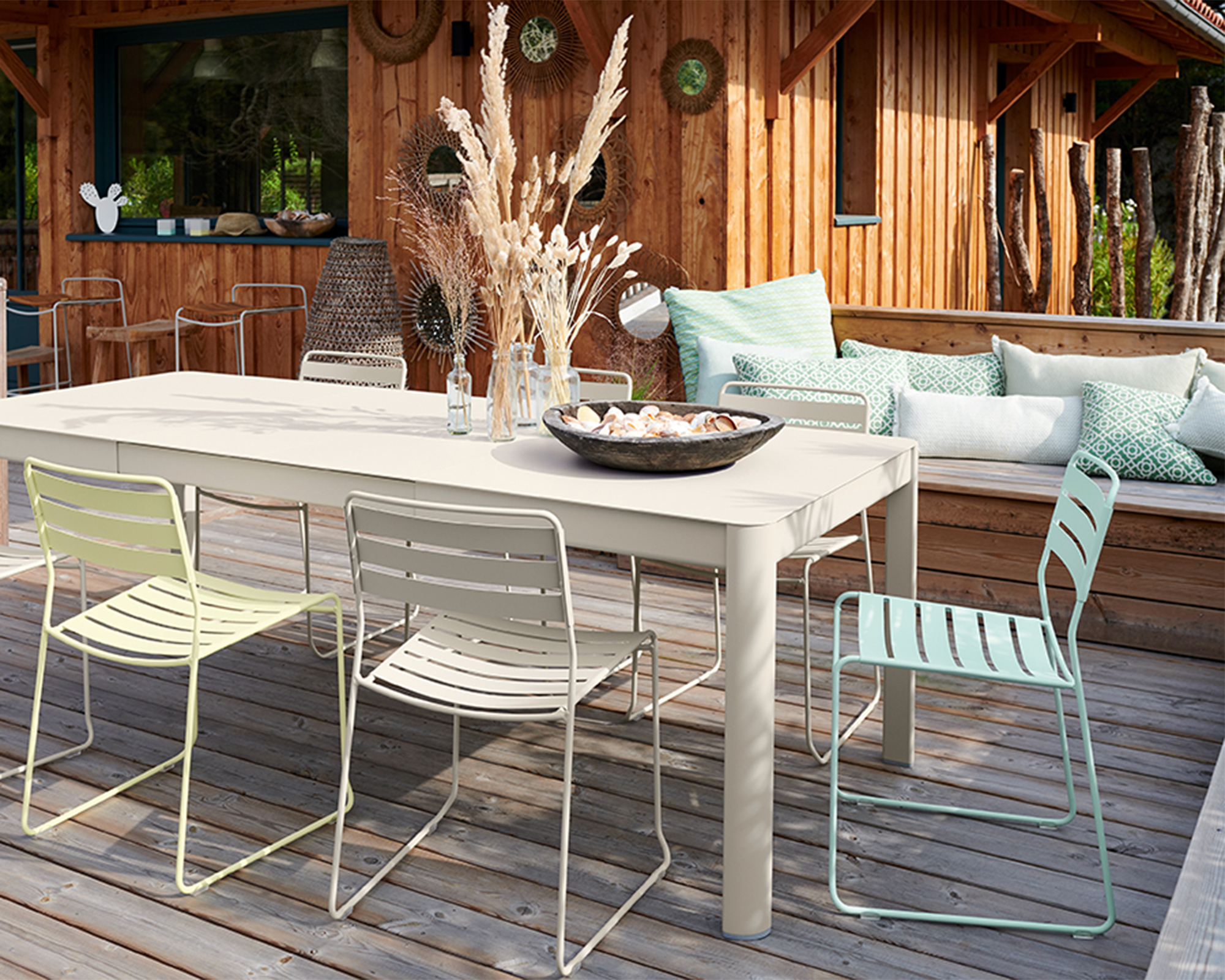 Decked area with pastel painted furniture in mint green and lemon yellow with cream dining tabled furniture