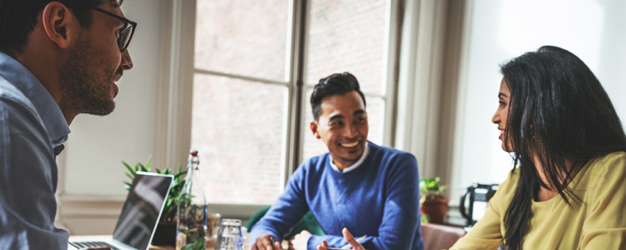 Two men and a woman of diverse ethnic backgrounds sitting at a conference table collaborating
