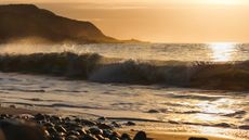 Photo of waves on a pebble beach at sunset (cropped to 16 by 9 format).