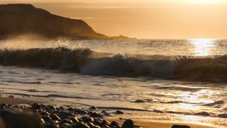 Photo of waves on a pebble beach at sunset (cropped to 16 by 9 format).