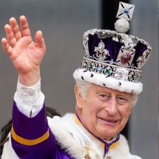 King Charles wearing a purple crown and robes waving on his coronation day 