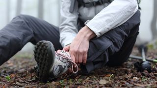 A hiker who has hurt their ankle sits down