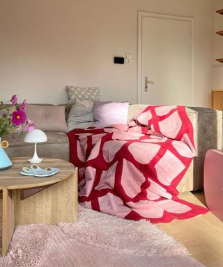 A gray couch with a red and pink blanket and a coffee table next to it