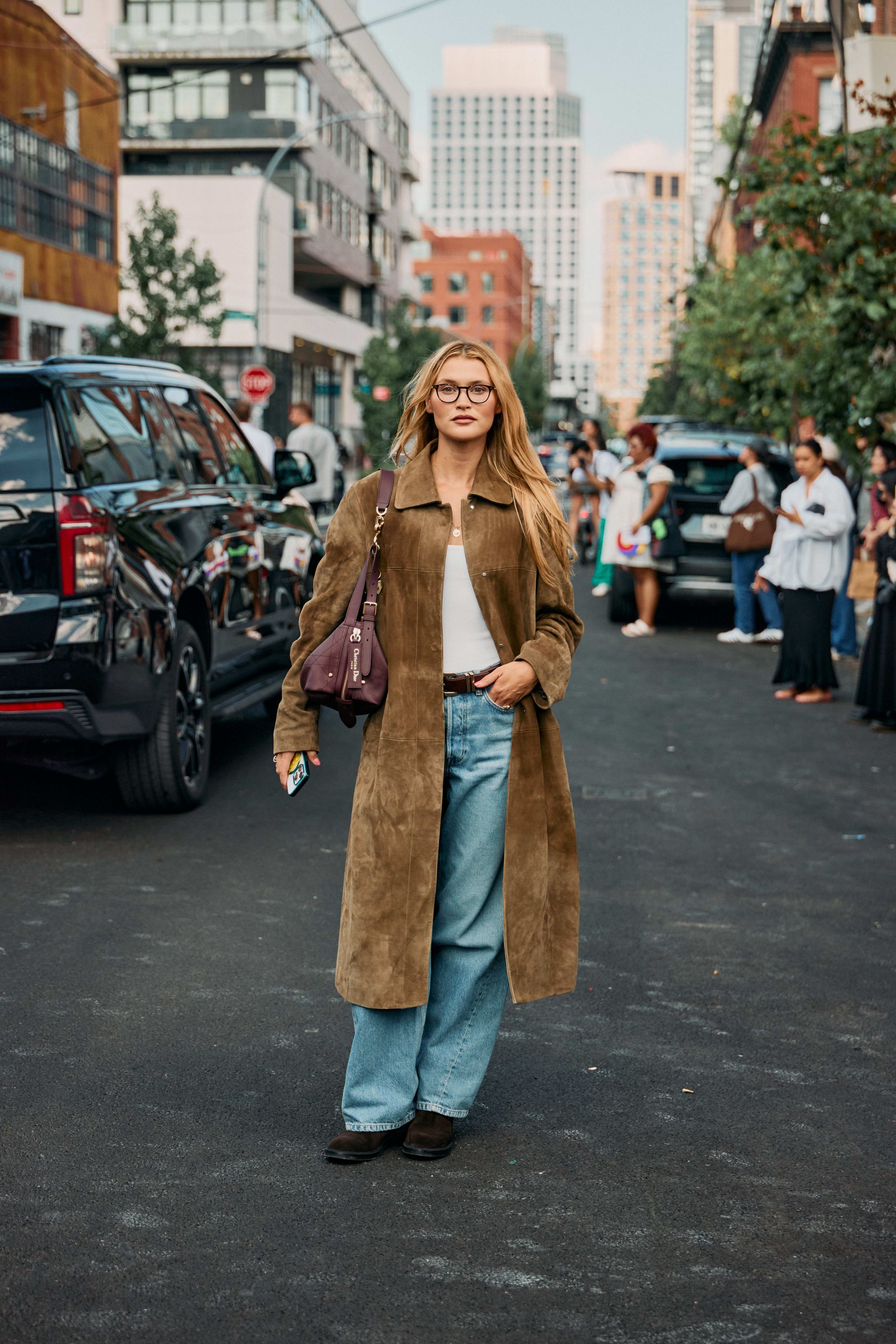 Woman in baggy light-wash jeans with moto-boots, white tank, and suede long coat.