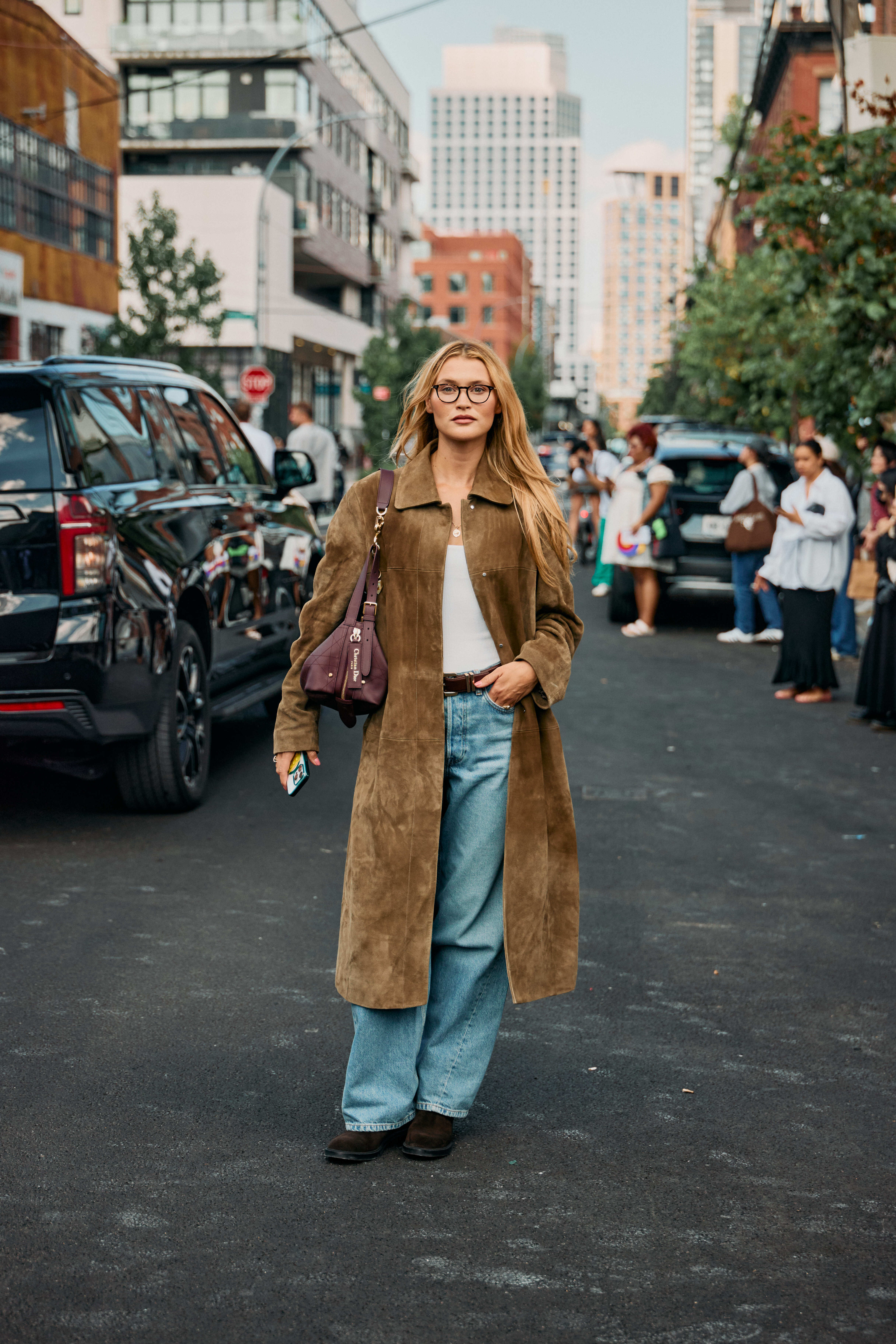 Woman in baggy light-wash jeans with moto-boots, white tank, and suede long coat.