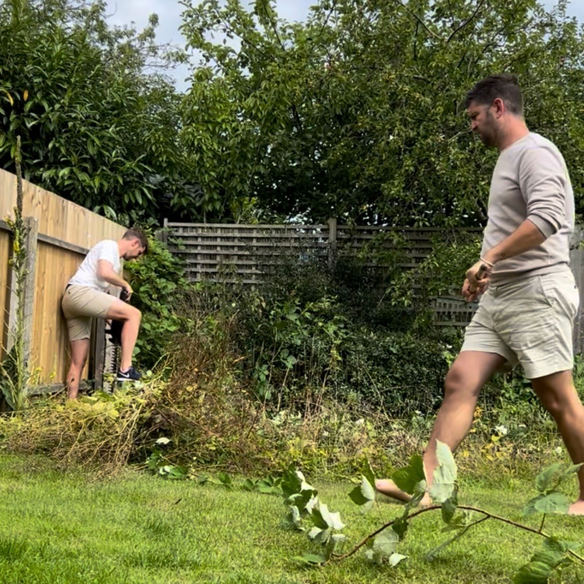 Two men in shorts walking in garden covered with weeds and garden debris