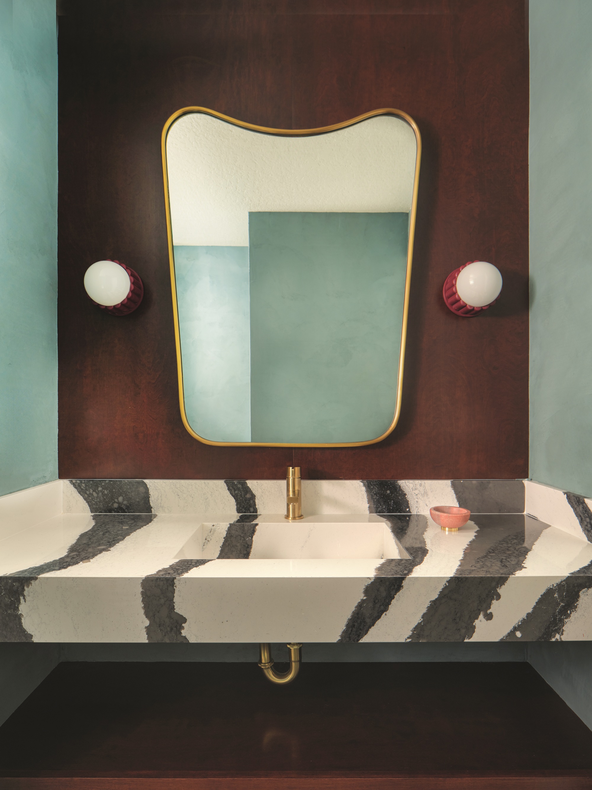 a bathroom with a black and white striped stone vanity and a mid century mirror