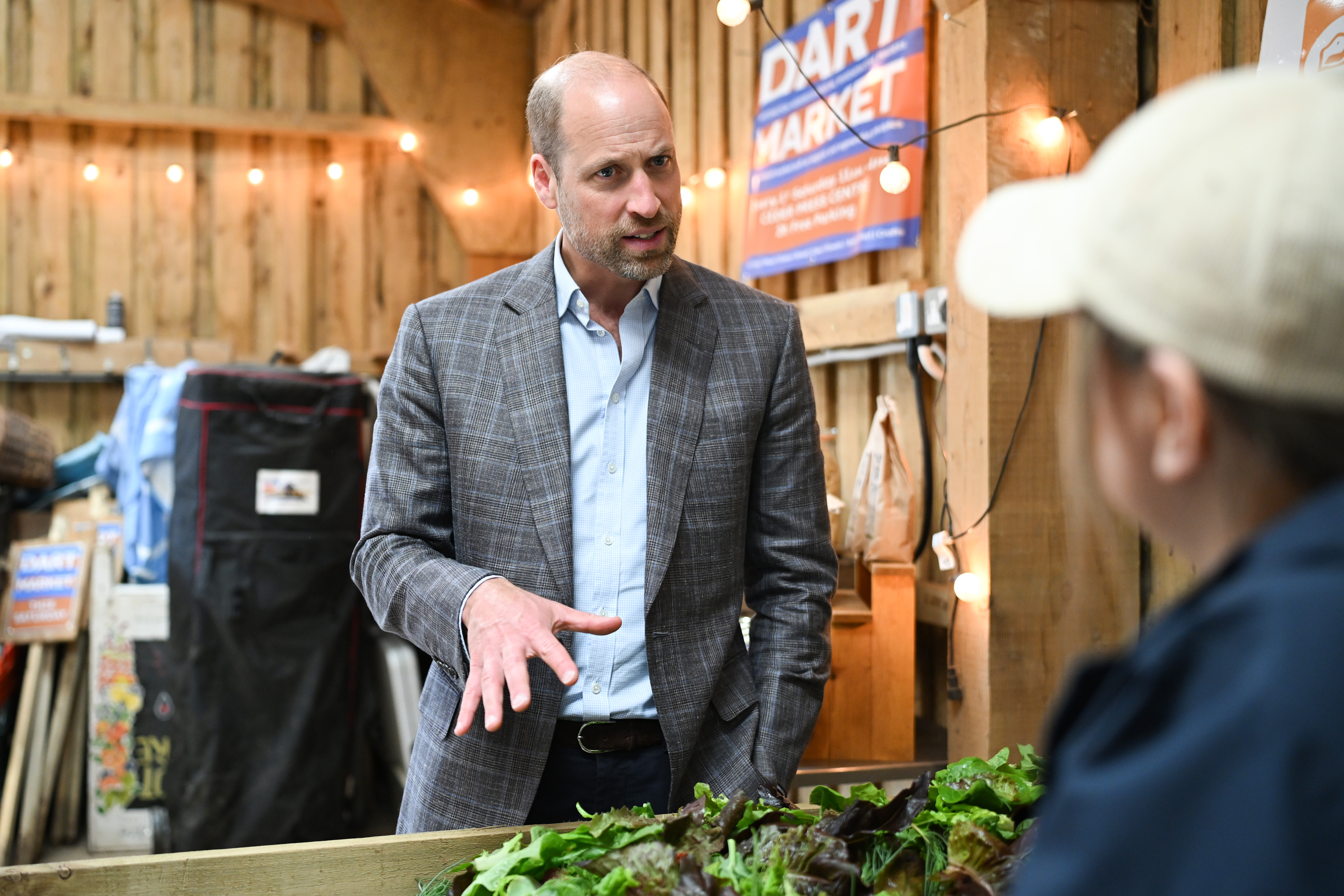 Prince William wears a gray plaid suit with a blue shirt and jeans while visiting the Apricot Centre, a carbon-negative farm and wellbeing service on June 18, 2026 in Totnes, England