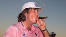 Neal Shipley wearing a pink polo and white cap while smoking a cigar