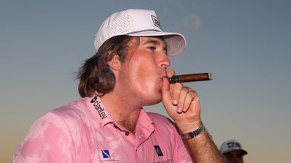 Neal Shipley wearing a pink polo and white cap while smoking a cigar