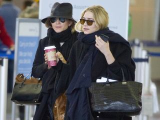 Mary-Kate and Ashley Olsen wearing layered winter looks at an airport with thick scarves and tucked-in hair.