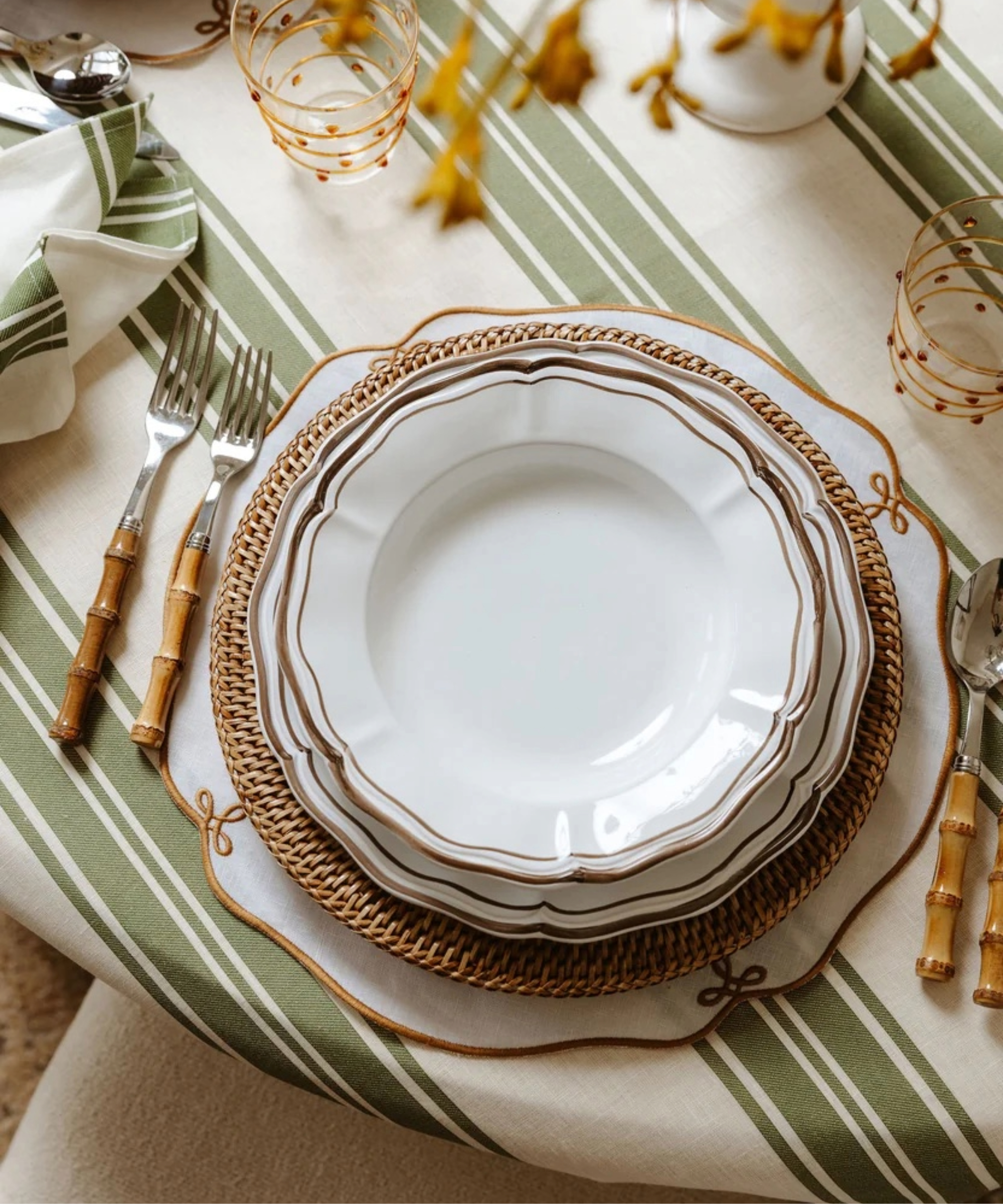green and white striped tablecloth with bamboo flatware, rattan placemats and scalloped plates