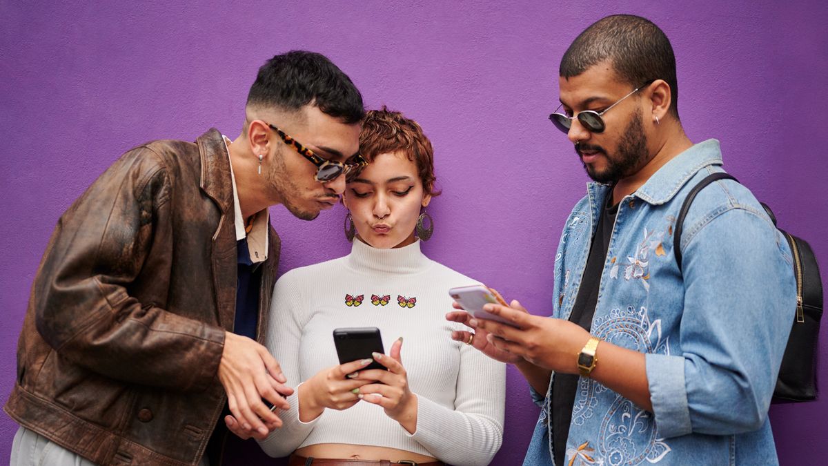 Group of diverse young friends checking their mobile phones together while standing in front of a purple wall